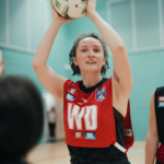 A netball player wearing a red bib labeled 