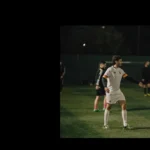 A group of soccer players on a field at night. Two players, one in a white uniform and the other in a red jersey, are engaged in a fist bump. Other players stand in the background near the goals. The field is dimly lit, emphasizing the players' actions—true teamwork found at careers at Powerleague.