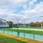 An outdoor 5-a-side football pitch with green turf and surrounding fences hosts local football leagues. A large white dome labeled 