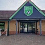 The entrance to the sports facility, home to local football leagues, features a triangular roof and a sign reading 